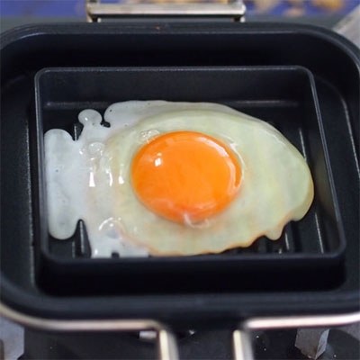 ホットパンに薄くサラダ油をしき、卵を割り入れる。溝に大さじ1の水を入れて蓋をし、中火と弱火の間で1分加熱したら本体をひっくり返し、さらに1分加熱して両面焼きの目玉焼きを作る