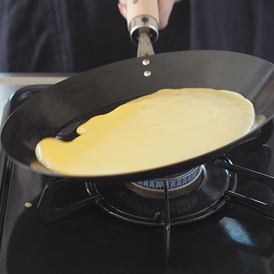 クレープ生地をお玉で軽く1杯分を流し入れ、フライパンを傾けながら手早く全体に広げます。火力は弱火で。