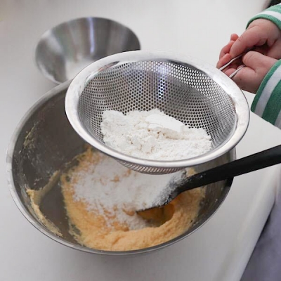 薄力粉とベーキングパウダーをふるいながら入れます。粉ふるい器があればベストですが、私の場合はザルでやっちゃいます。娘に手伝ってもらったら粉がこぼれました・・・