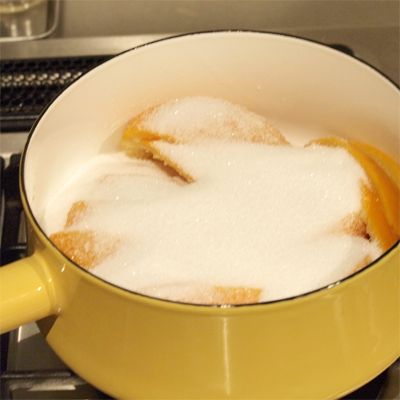 2度目ゆでこぼして、水に入れて冷やし、ざるにあけて水気を切り、軽く押さえるようにして更に水気を切る。皮の重さを量りグラニュー糖の量を計算する(皮の重さの60～70%)。