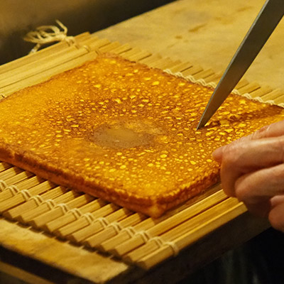 熱いうちにオニスの上に最初に焼いた面を下にして置き、巻いたとき綺麗な形になるように、包丁でオニスの線に沿って浅く切り込みを入れます。