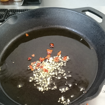 「ロッジ　スキレット　10　1/4インチ」にオリーブオイルをたっぷりと注ぎ、にんにくと赤唐辛子を入れ、火をつけて香りがたったら塩小さじ1を入れる